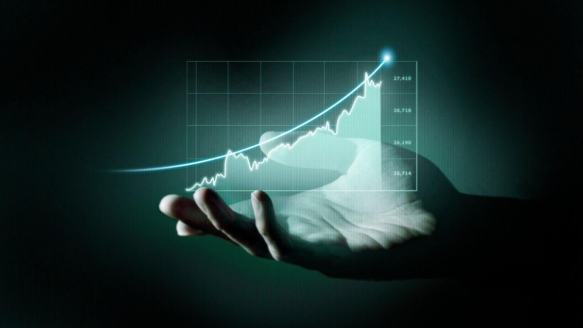 Hand under a glowing holographic stock chart showing an upward financial trend and rising values on the right.