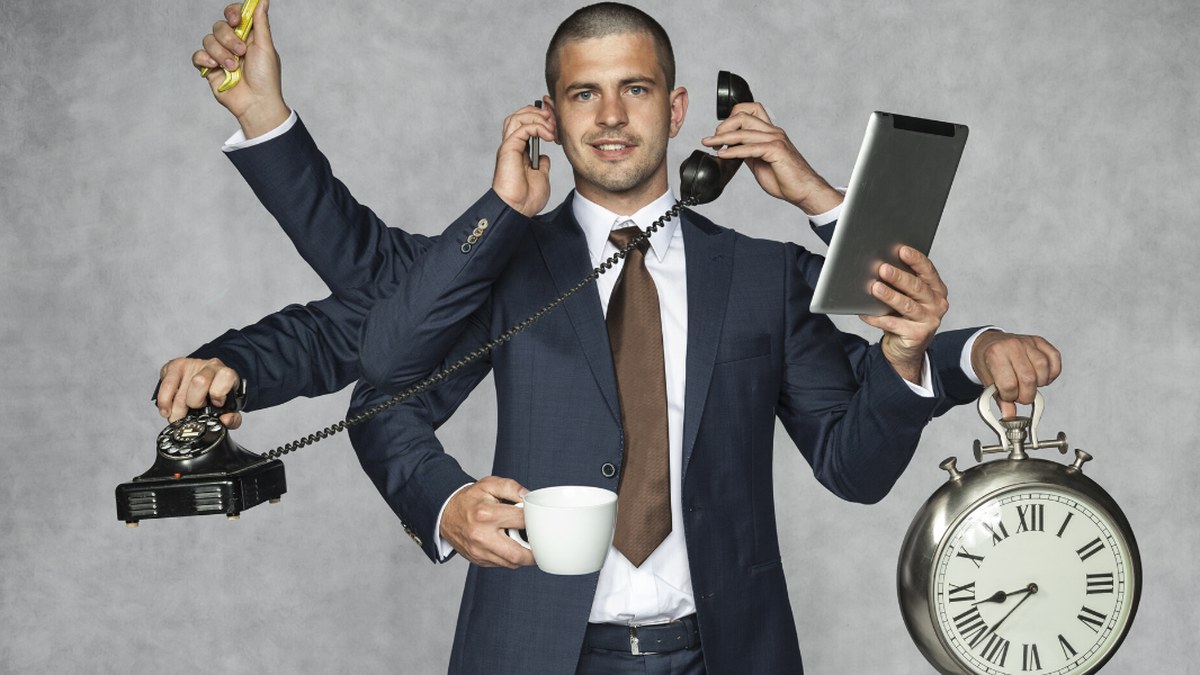 Businessman in a suit with multiple arms juggling tasks: talking on a corded phone, holding a tablet, a coffee cup, and a large clock symbolizing time management.