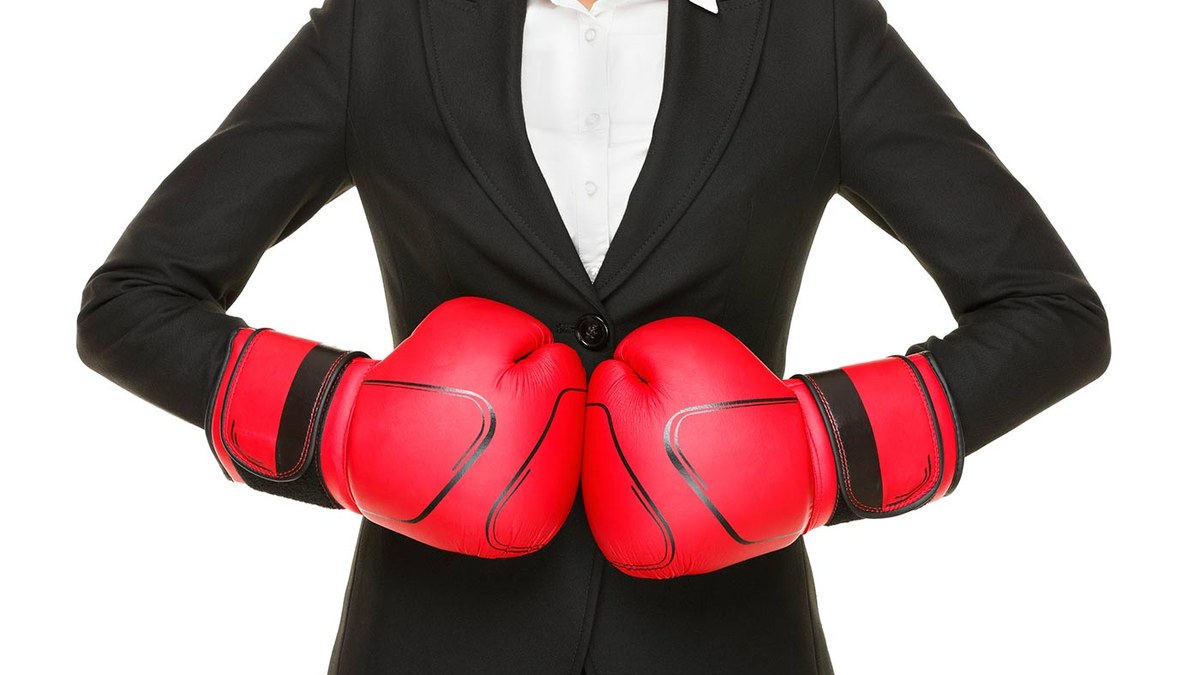 Person in a black suit and white shirt wearing red boxing gloves, fists pressed together at the chest.