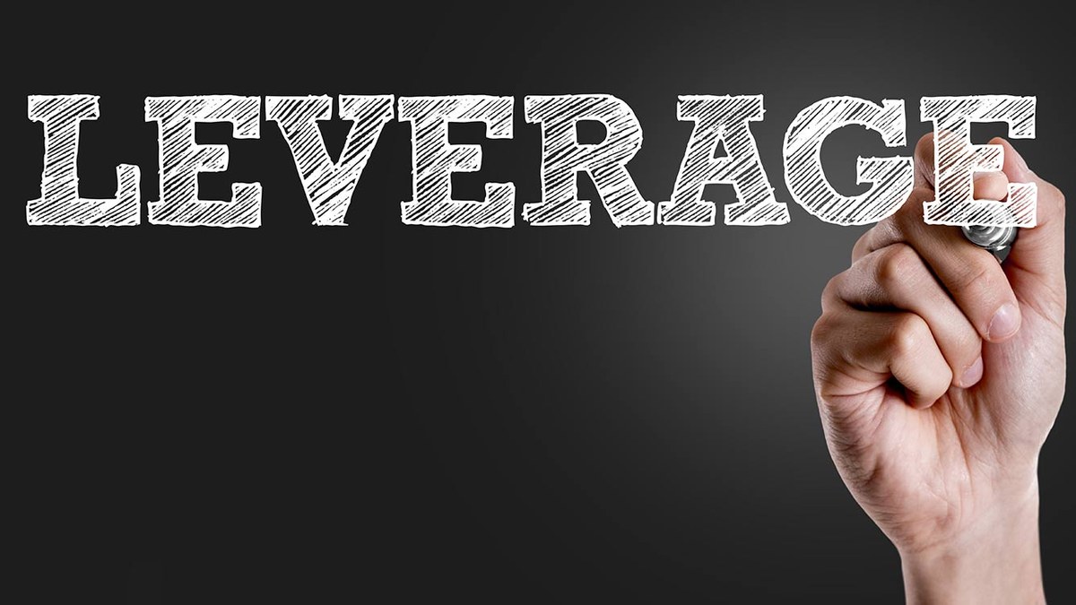 Chalk-drawn word LEVERAGE on a dark background with a hand holding chalk near the end of the word.
