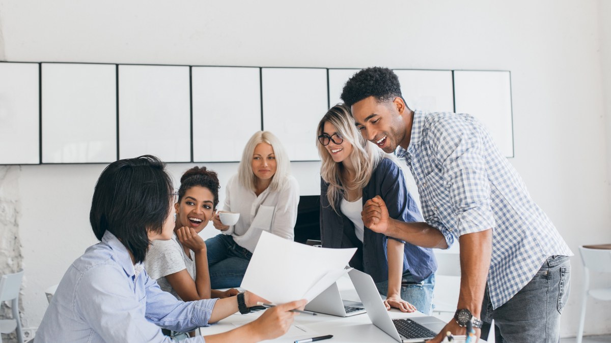 A diverse group of coworkers collaborating around a table, reviewing documents and a laptop with smiles and engagement.