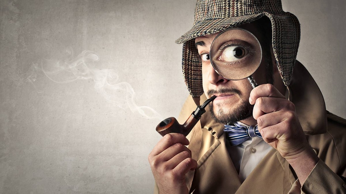 Man dressed as a detective looks through a magnifying glass, holding a smoking pipe.