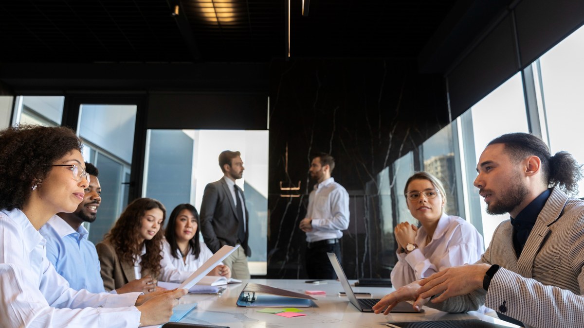 Group of diverse professionals in a boardroom, discussing with laptops and documents on the table.