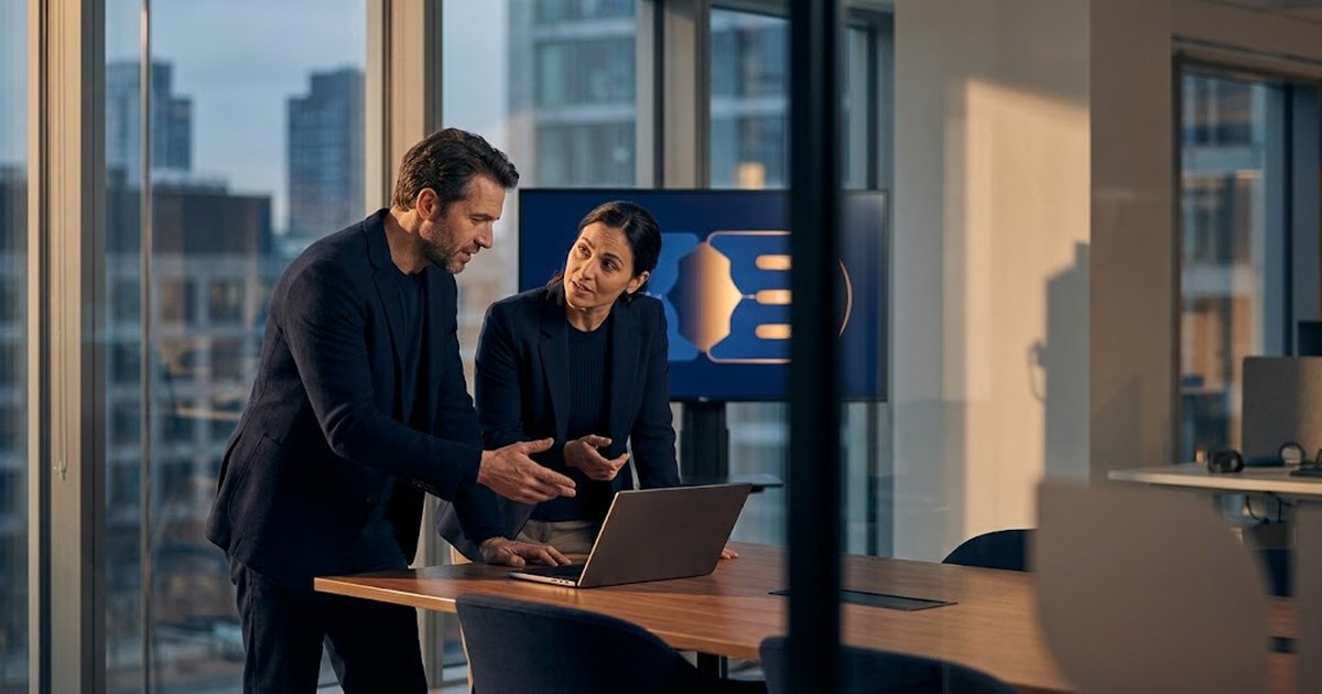 Two revenue leaders comparing partner enablement software options on a laptop in a glass-walled meeting room