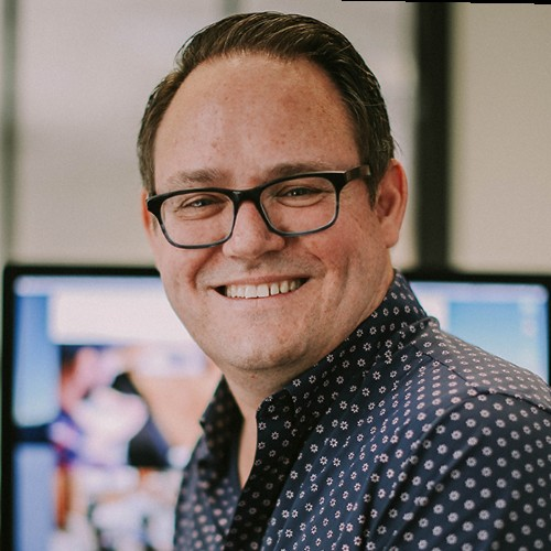 Portrait of a smiling man wearing glasses in an office setting, facing the camera.