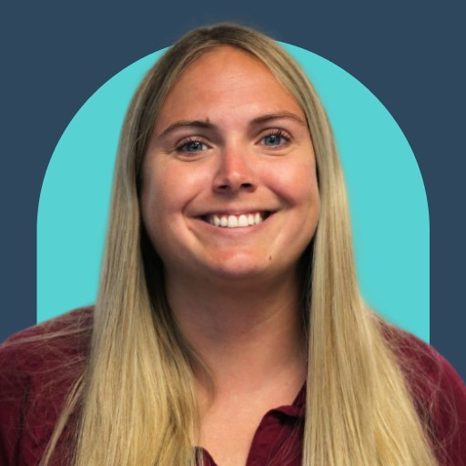 Portrait of a smiling woman with long blond hair, wearing a maroon top, against a teal circular backdrop on a dark blue background.
